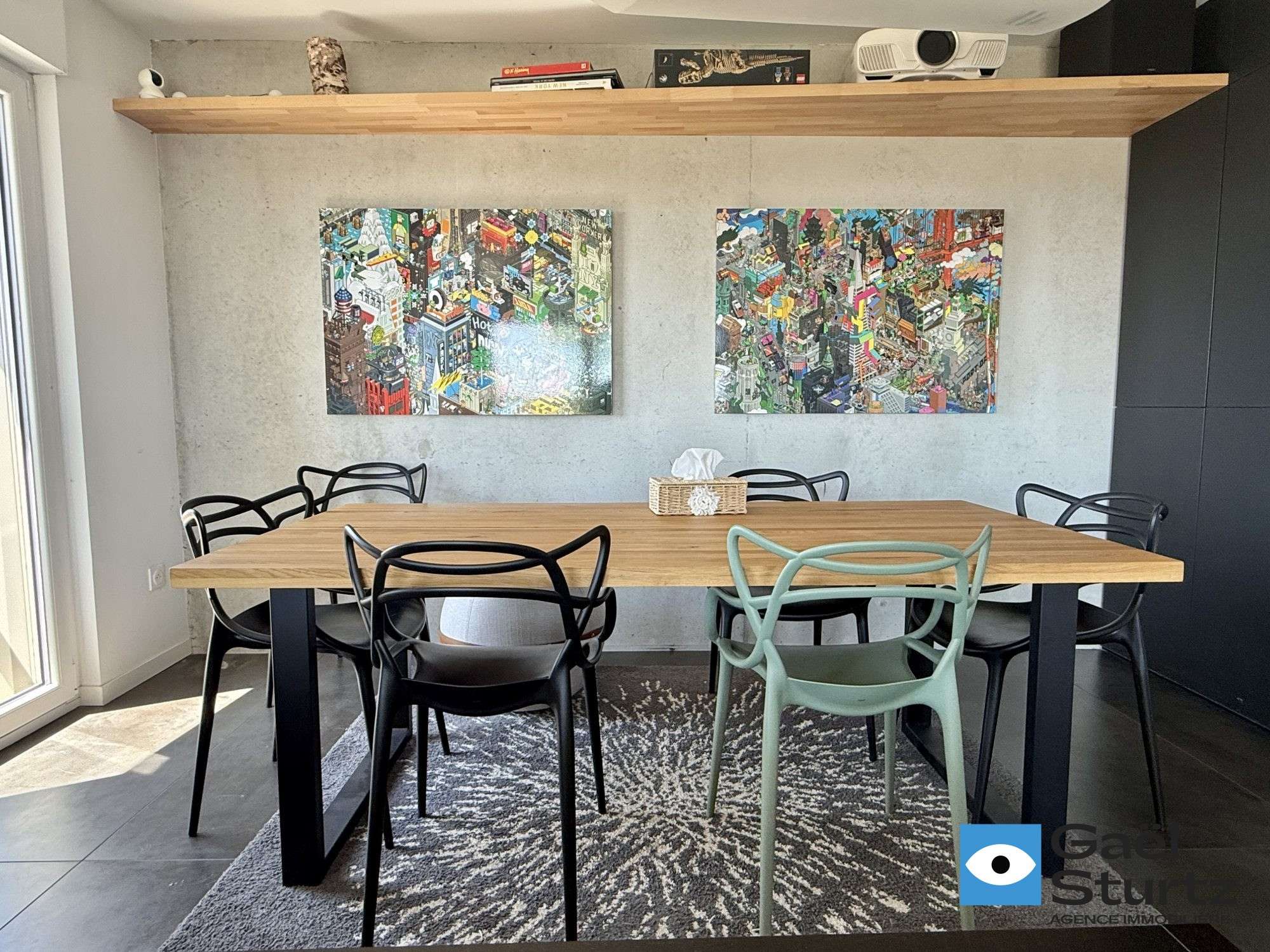 Table de la salle à manger, chaises et tableaux colorés au mur.