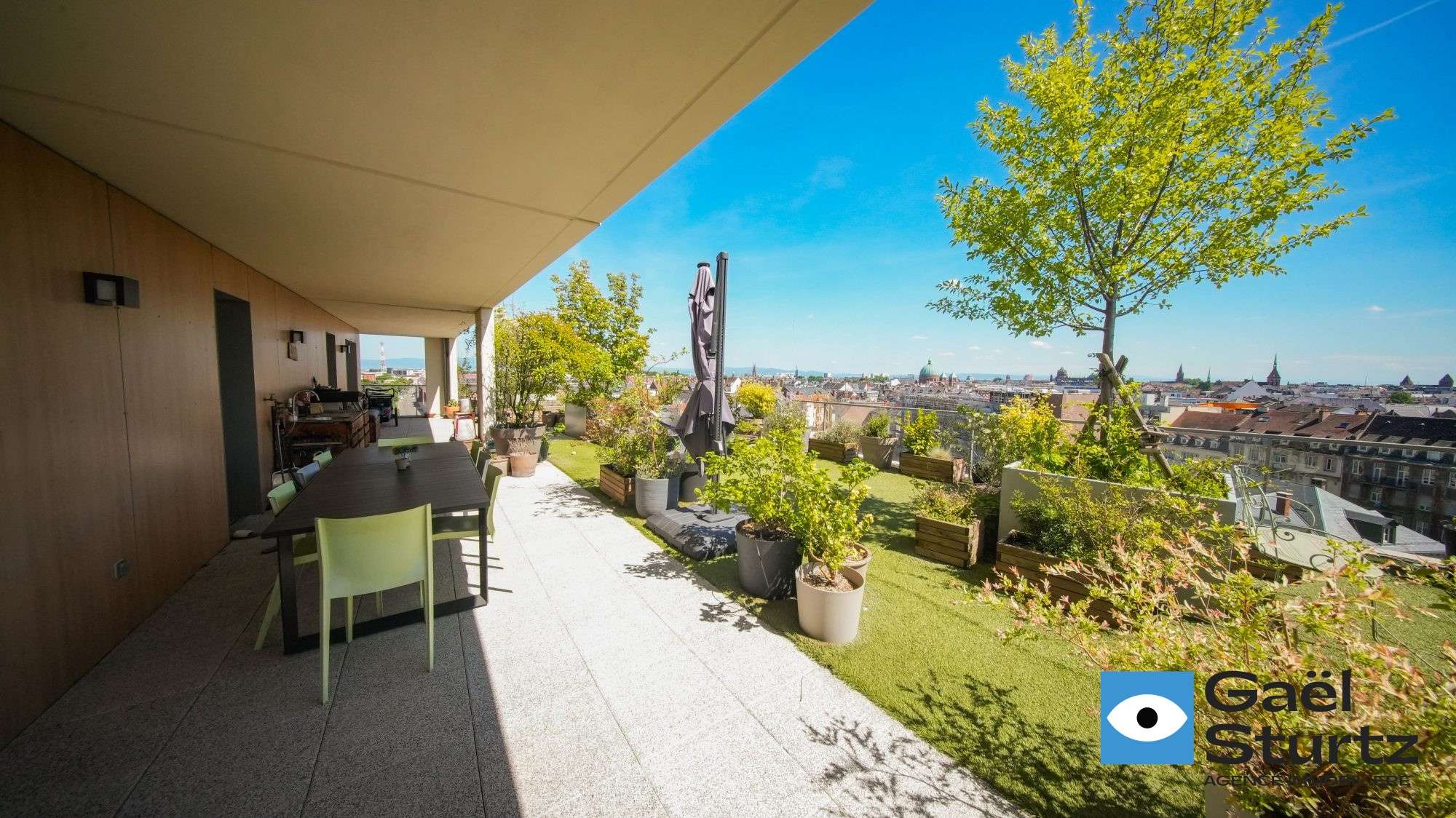 Table sous l’avancée du bâtiment et terrasse végétalisée.