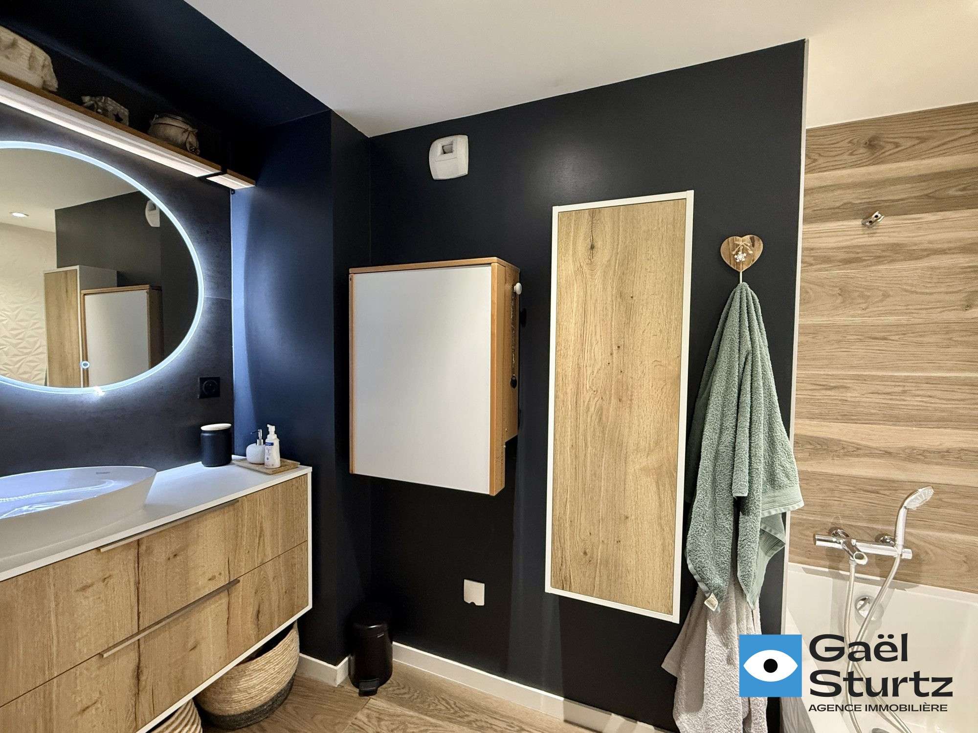 Salle de bains avec meuble vasque, miroir rond et baignoire.